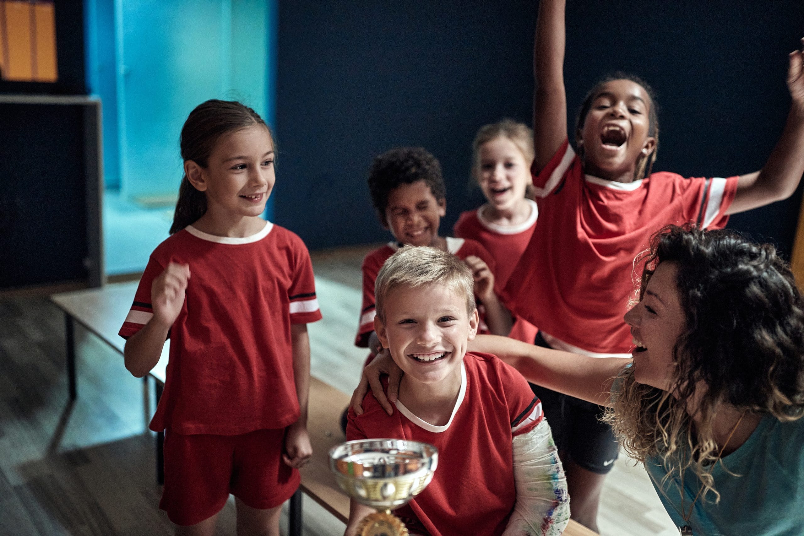 Kids team and female coach posing with won trophy. Children team sport Kids team and female coach at the locker room posing with won trophy. Children team sport